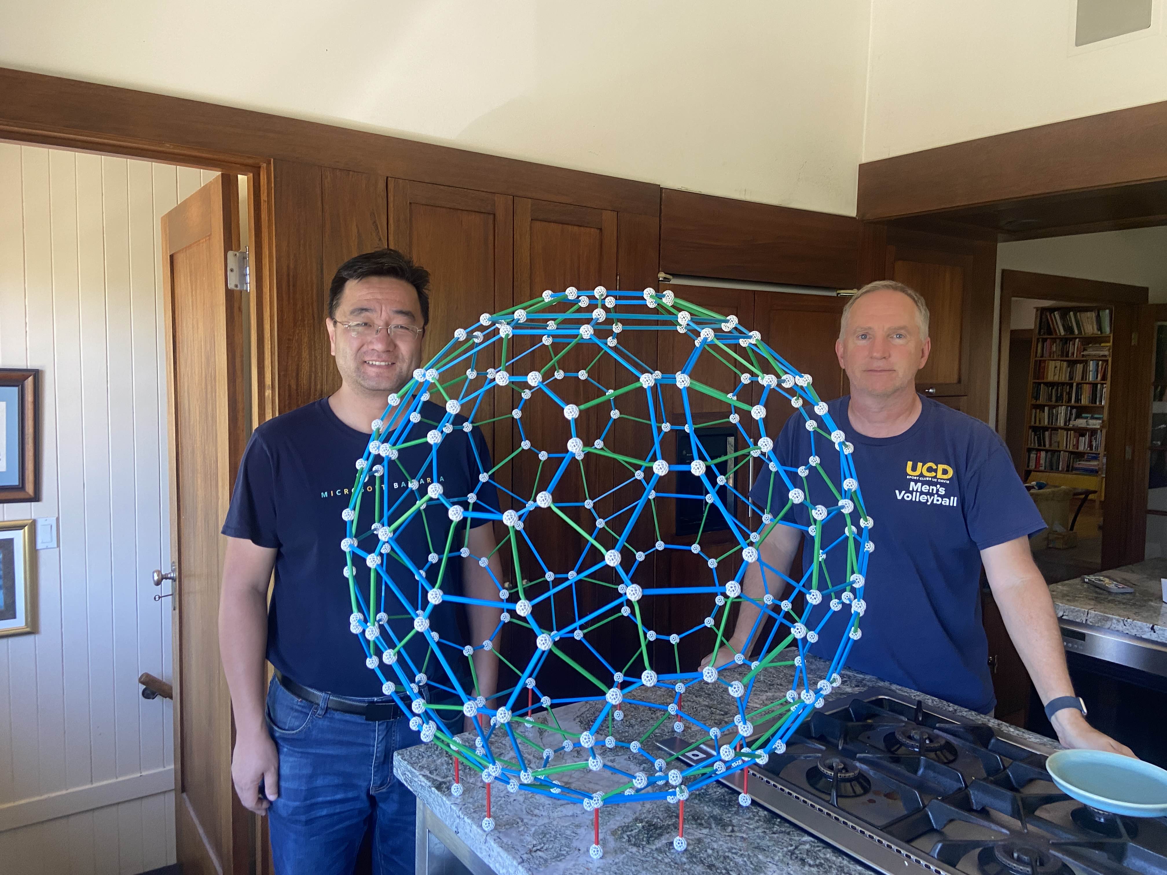 Two builders beside the completed blue-and-green 240-ball Zometool shell